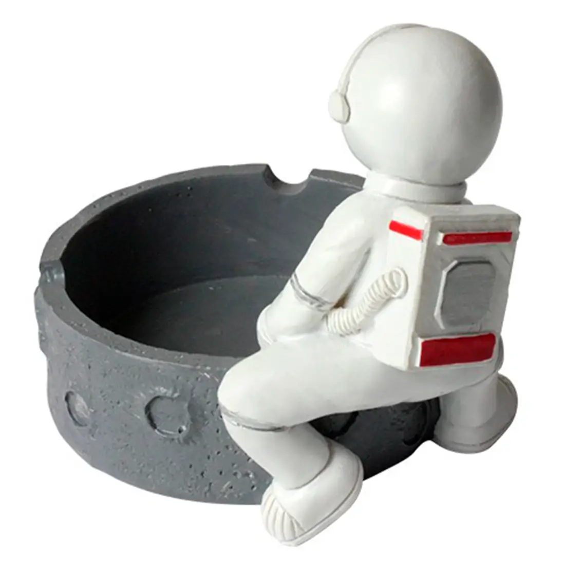 Ashtroen har en skulpturel udformning af en astronaut i en lys metallic farve med detaljerede elementer som hjelm og dragt. Den har en glat overflade med skarpe linjer og en struktureret base, der giver stabilitet. Astronautens hænder er strakt ud, mens skålen til aske er placeret i midten, hvilket skaber en visuel balance og funktionalitet.