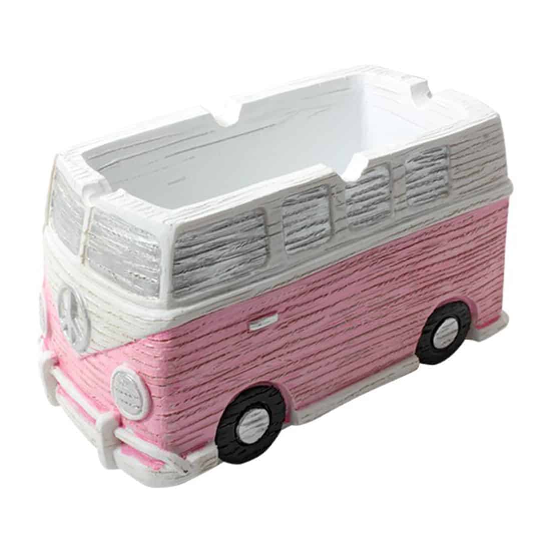 Et askebæger i form af en klassisk VW bus pryder overfladen med en lys pink farve. Bilen har detaljer som hvide vinduer og sorte dæk, der tilføjer kontrast. Formen er rundet med bløde kanter, og der er synlige udskæringer til askebægerets funktion. Bunden er flad, hvilket sikrer stabilitet. Den legende design skaber en iøjnefaldende dekoration.