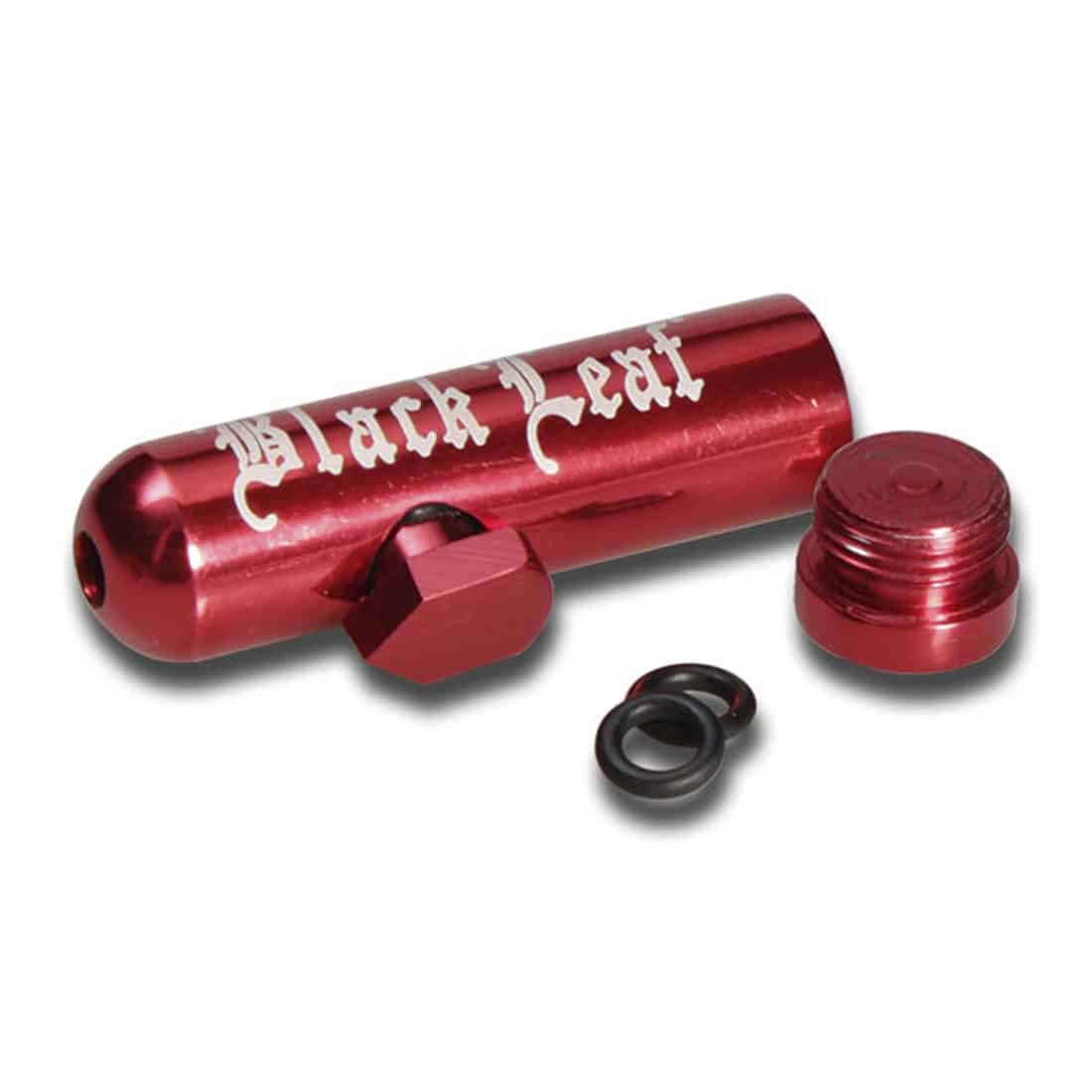 Sort bladformet enhed med en glat overflade og en let buet profil. Den har en rød knap placeret centralt på fronten, omgivet af en sort ramme. Enheden har små ventilationshuller på siderne. Materialet synes at være plastik med en mat finish. Baggrunden er ensfarvet og neutral for at fremhæve enheden.