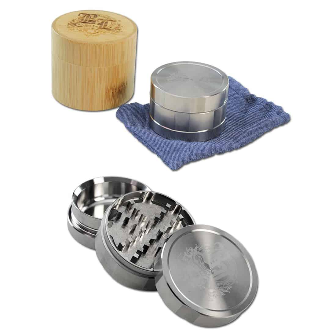 En sort, bladformet krydderikværn i rustfrit stål med tre dele præsenteres. Overfladen har en glat, mat finish, mens det øverste låg har et diskret bladmønster. Kværnen har en diameter på 59 mm og er udstyret med en skarp, tandet inderside til effektiv kværning. Den er designet med en skridsikker bund for stabilitet.