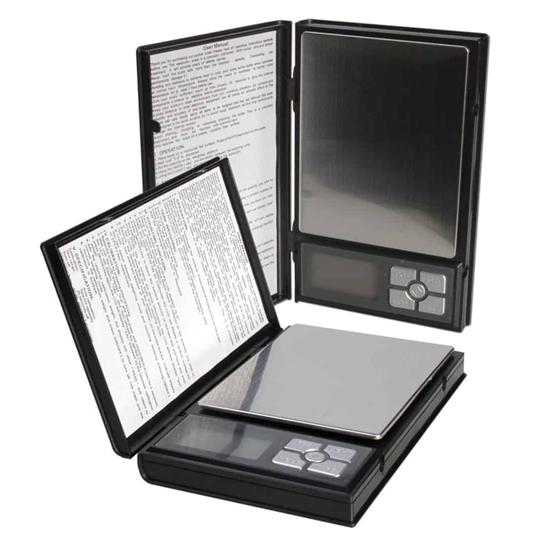 En sort notesbog med en blød overflade og en enkelt, synlig rygsøm. Foran er der en sølvfarvet metalclip, som holder en stk. papir indeni. Notatbogen hviler på en grå overflade, mens der i baggrunden ses en vægt med en tydelig digital skærm, som viser tal i lysende blå.