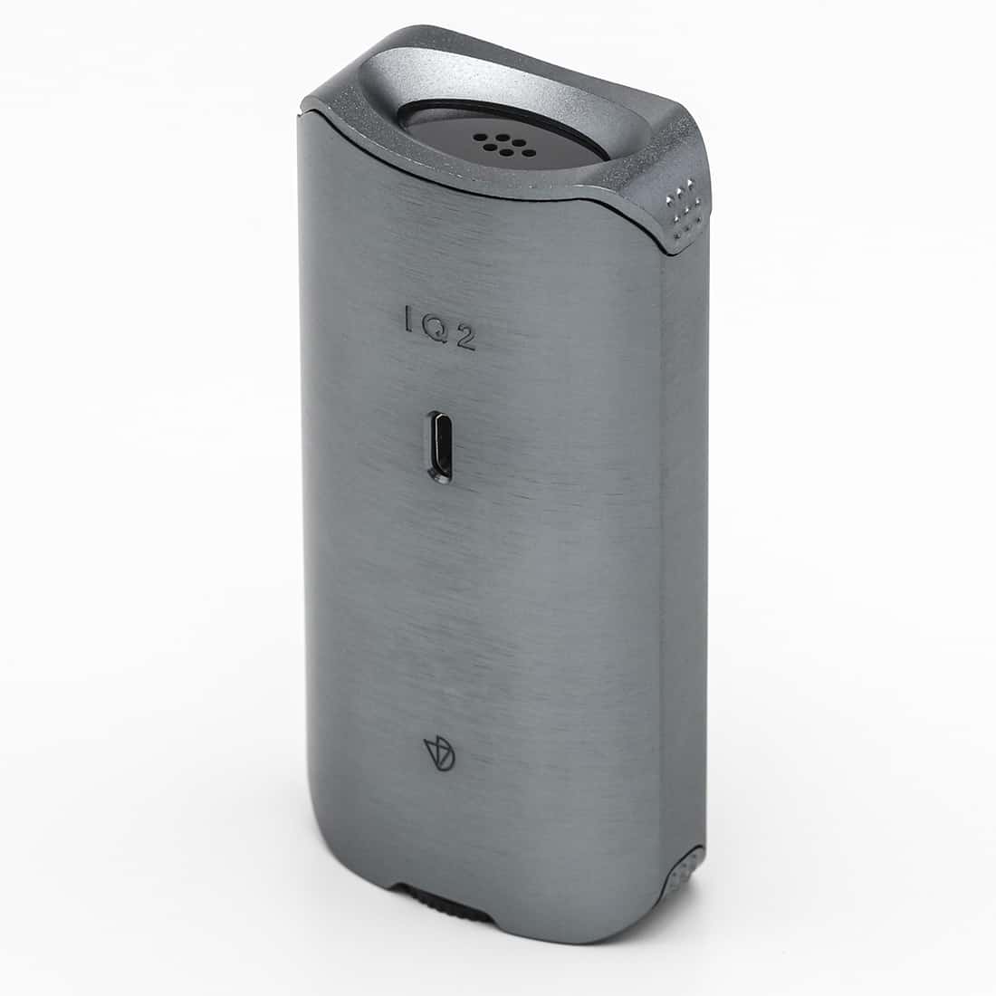 En kompakt vaporizator præsenterer sig i en mørkegrå, mat finish. Den har en strømlinet form med bløde, afrundede kanter. Fronten er udstyret med et digitalt display og knapper til temperaturjustering. En slim, let buet mundstykke er placeret øverst, mens en perforeret sektion på siden giver et moderne touch. Materialet fremstår robust og holdbart.