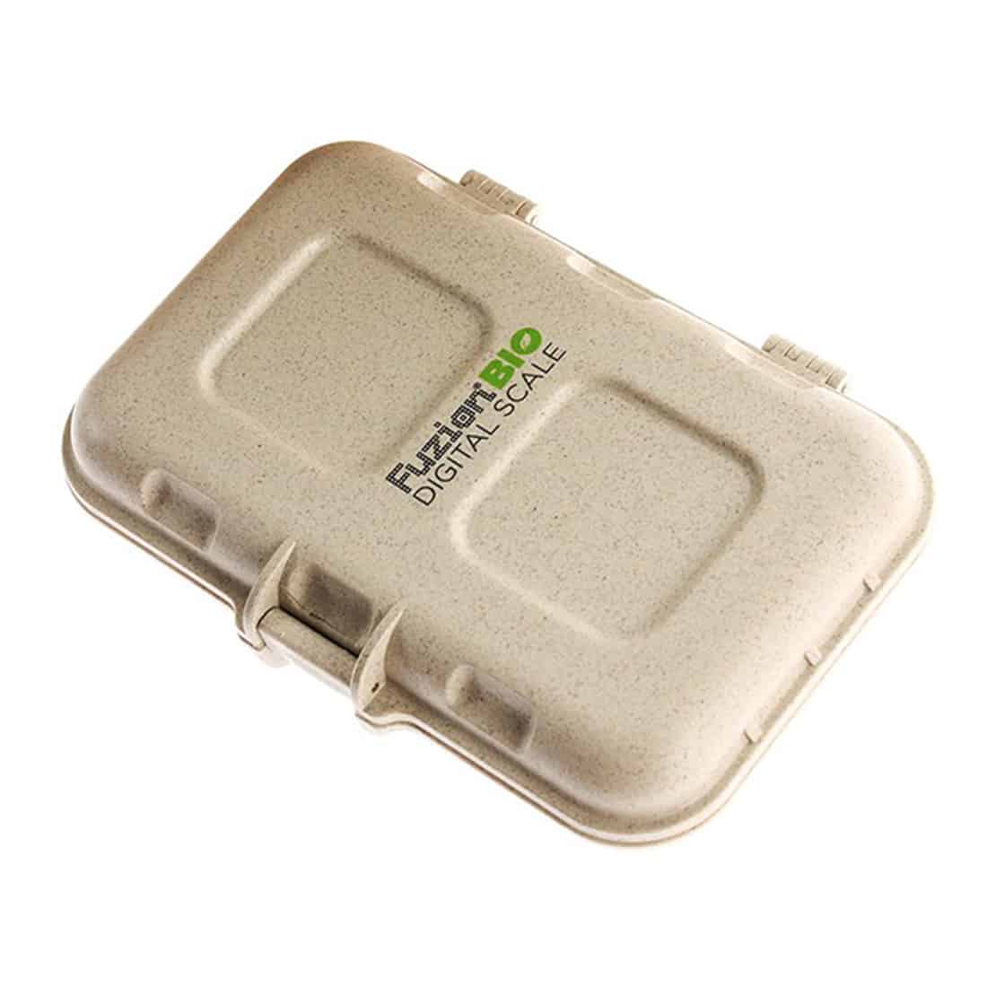 En hvid, cylindrisk beholder med en skruehætte pryder midten af kompositionen. Beholderens overflade er glat og skinner let, hvilket indikerer et plastmateriale. På etiketten er der et farverigt design med grønne og orange nuancer, der indeholder tekst i sort. Nederst er der en detaljeret liste af ingredienser samt en vægtangivelse på 20 gram.