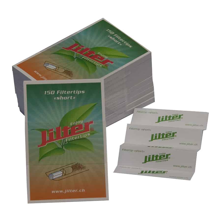 En pakke med filtertips præsenteres i en rektangulær form, dækket af en farverig, illustreret emballage. Farverne domineres af lyse nuancer af grøn, gul og rød, med detaljerede mønstre og grafik. På emballagen ses tekst i hvid og sort, der angiver produktinformation. Filtertipsene er synlige gennem en åben sektion, tydeligt adskilt og organiseret.