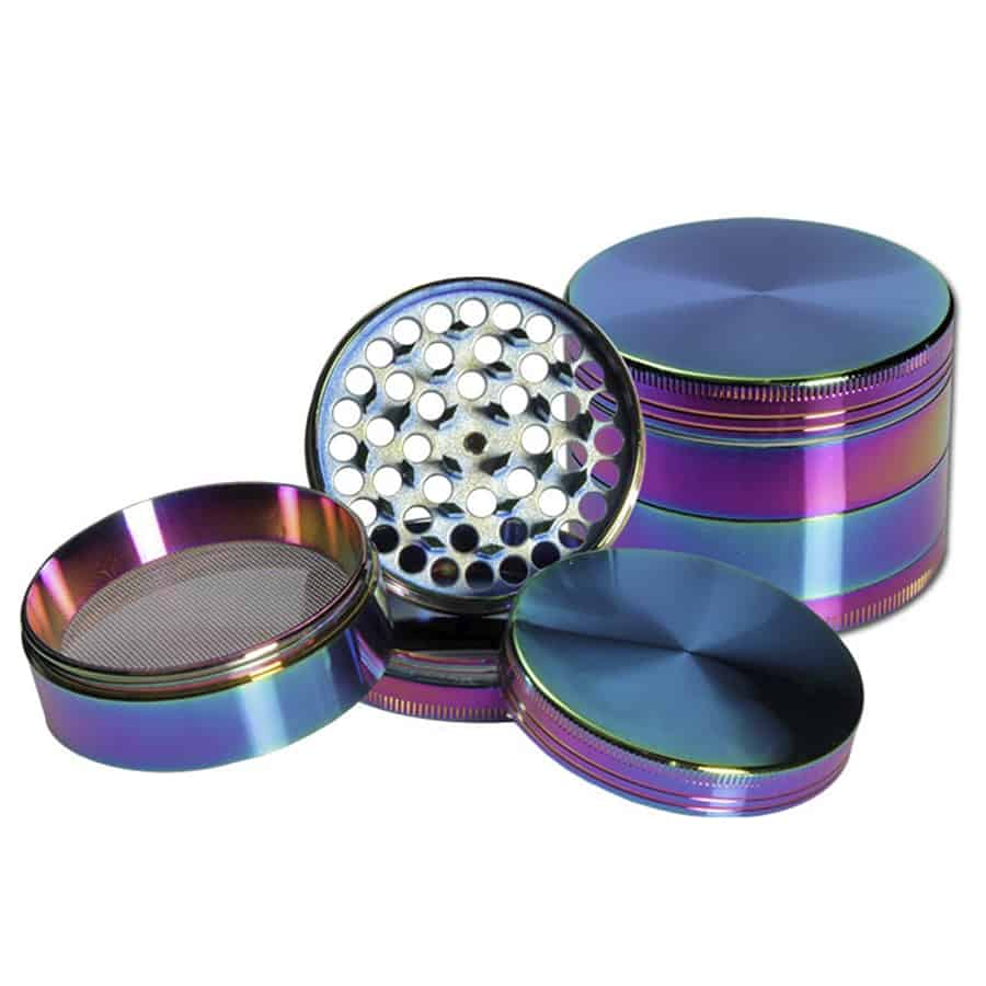 En metalgrinder præsenterer sig med en rund, flad form og en glat overflade i nuancer af oliefarver, der skaber en iriserende effekt. Den har en skruelås, der sikrer tæt lukning, og tænderne indeni er skarpe og geometrisk formede for optimal funktion. Overfladen reflekterer lys, hvilket fremhæver de forskellige farvetoner og skaber dybde.