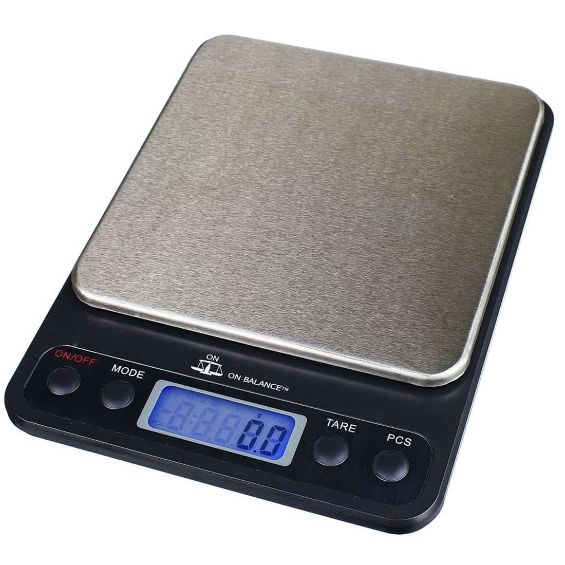 En vægt med en metalbund og en klar, glasagtig skål er placeret på en flad overflade. Vægten har en skala med tal og markeringer i sort, som tydeligt viser målinger. Skålen er fyldt med en grålig substans, der har en grov tekstur. Baggrunden er lys og neutral, hvilket fremhæver vægtens detaljer.