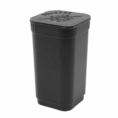 En firkantet, sort emballage med en glat, mat overflade. Forsiden prydes af en hvid tekst med en tydelig skrifttype, der angiver produktinformation. Kanten er skarpt afgrænset, og emballagen er lukket med en metalplade, der giver en let refleksion. Baggrunden er lys, hvilket fremhæver den mørke farve og de kontrasterende detaljer.