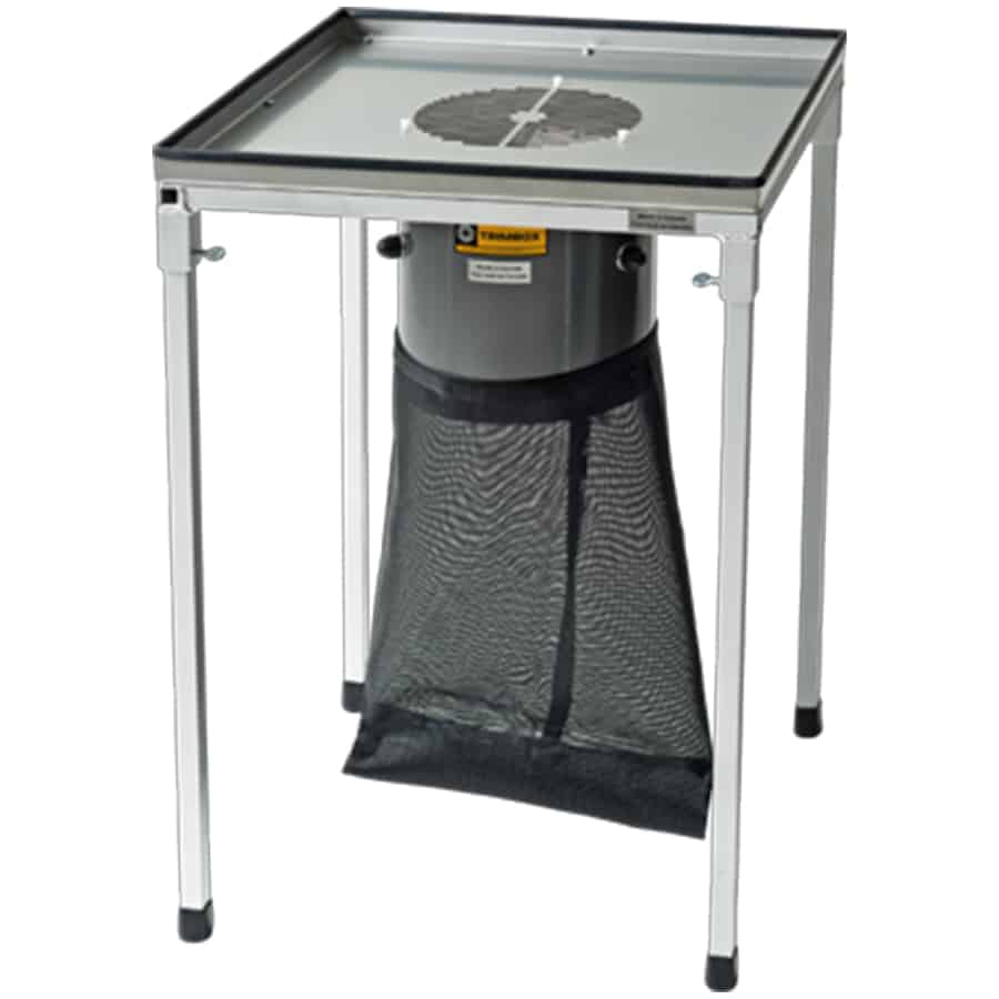 En arbejdsstation med en rektangulær form, fremstillet af metal og plast. Overfladen er dækket af en grå tekstur, og der er synlige knapper i sort. En arbejdsflade er placeret centralt, omgivet af flere opbevaringsrum med lukkede låger. En ledning er synlig i bunden, og der er små hjul, hvilket muliggør mobilitet.