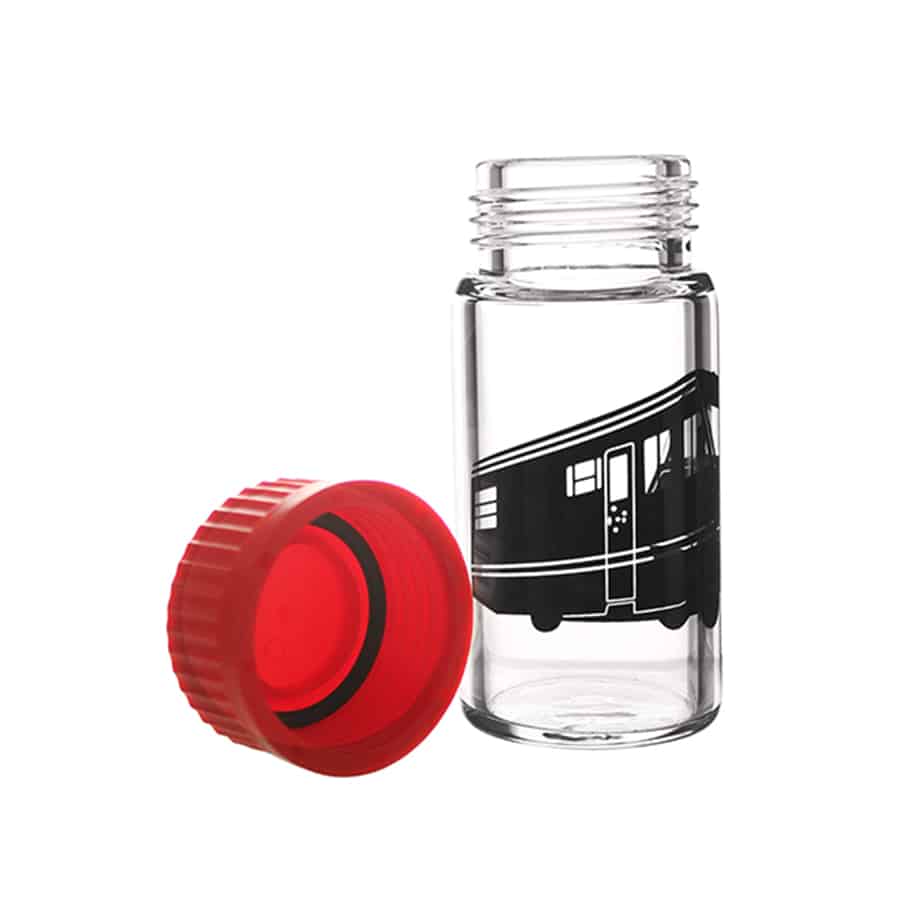 En klar glasbeholder med en sort gummipakning i toppen. Beholderen har en cylindrisk form og en glat overflade, hvilket giver et elegant udtryk. På låget er der en enkelt, lille, rund knap i metal, der fungerer som lukkeanordning. Den transparente glasstruktur afslører indholdet, der fremstår i forskellige nuancer af grønne og brune farver.