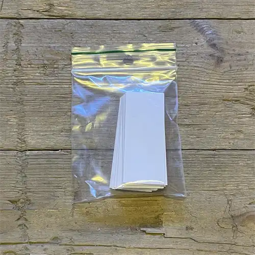 Hvide filtertips i en lige, cylindrisk form, pakket i en transparent plastikpose. Hver filtertip har en glat overflade med en lille diameter, og de er ensartede med en let skinnende finish. Posens design inkluderer en klar lukning og en etiket, der angiver antallet af filtertips, som er 50 stk. Placeringen af filtertipsene fremhæver deres ensartethed.