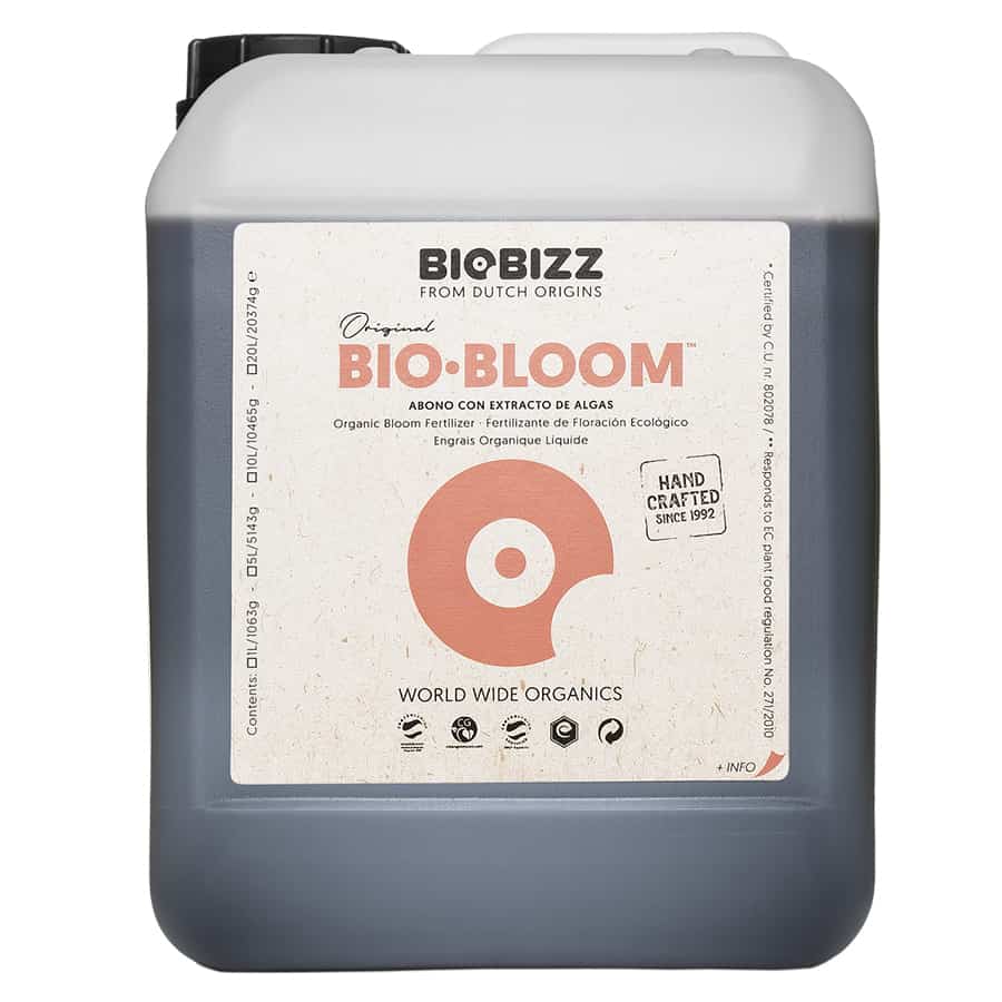 En transparent plastflaske med en grøn etiket pryder overfladen. Flasken har en slank, cylindrisk form og en sort skruelåg. Etiketdesignet inkluderer hvid tekst samt et grønt og gult mønster med blomsterelementer. Indholdet er en brunlig væske, der fylder omkring tre fjerdedele af flasken, hvilket skaber en let refleksion på overfladen.