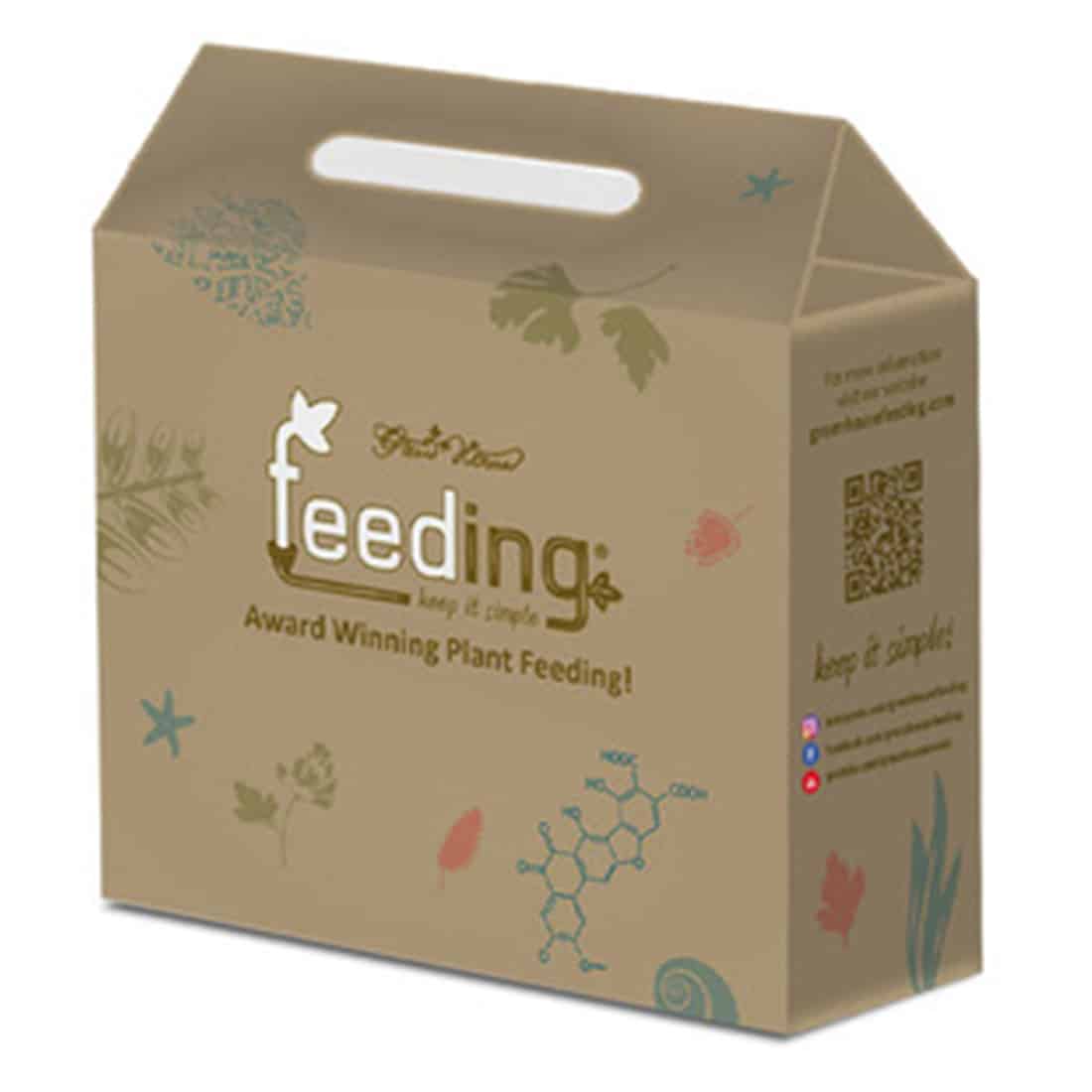 Et grønt plastikhus med en gennemsigtig, kuppelformet top dominerer scenen. Huset hviler på en mørk, glat overflade. Indvendigt ses flere små, aflange potter i forskellige størrelser, der er fyldt med jord. Potterne har runde former og er placeret i et systematisk mønster. Der er et skilt med tekst i øverste venstre hjørne.