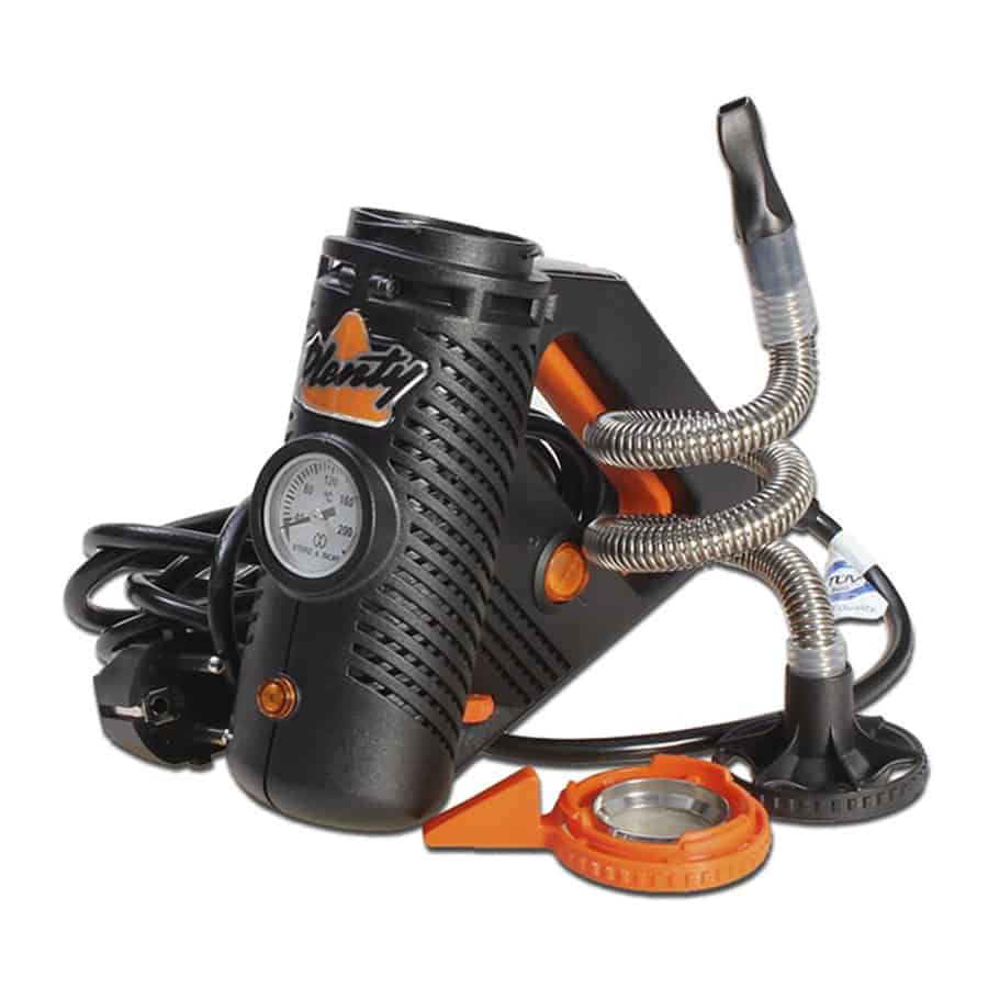 En åbent designet vaporizer i en slank, moderne form. Den er fremstillet af metal med en børstet overflade, der giver en mat finish. En gennemsigtig kappe afslører det indre, hvor et varmeelement og en lille skål er synlige. Der er en diskret knap til betjening og et LED-lys, der indikerer enhedens status. Farverne er neutrale, primært i grå og sort.