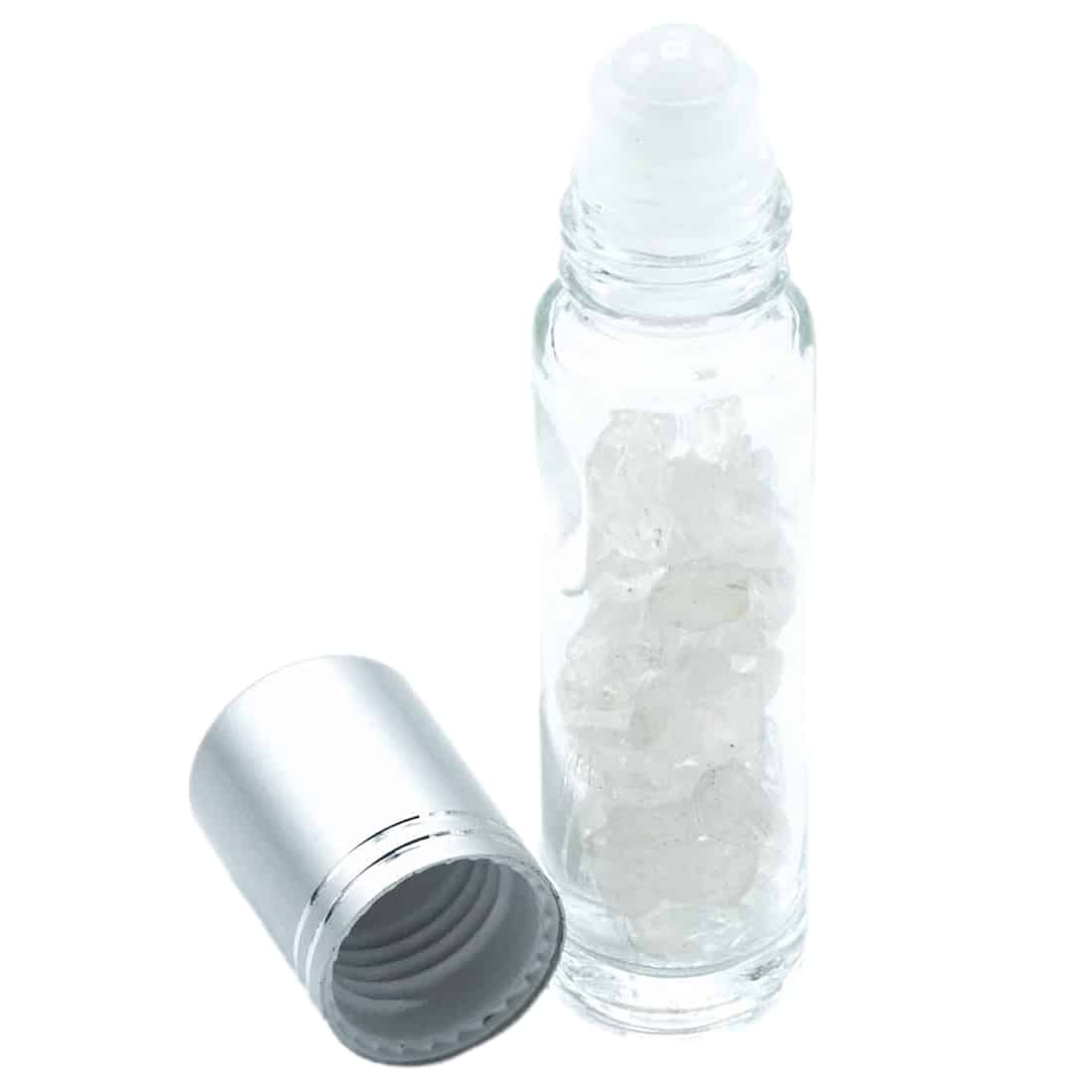 En transparent rollerflaske i glas pryder en hvid overflade, med en cylinderformet krop og en glat, skinnende overflade. Flasken har en gylden metalrulle og en sort hætte, der afslutter toppen. Indholdet er en lys, næsten farveløs væske, der reflekterer lyset svagt, mens flaskens elegante design skaber et minimalistisk udtryk.