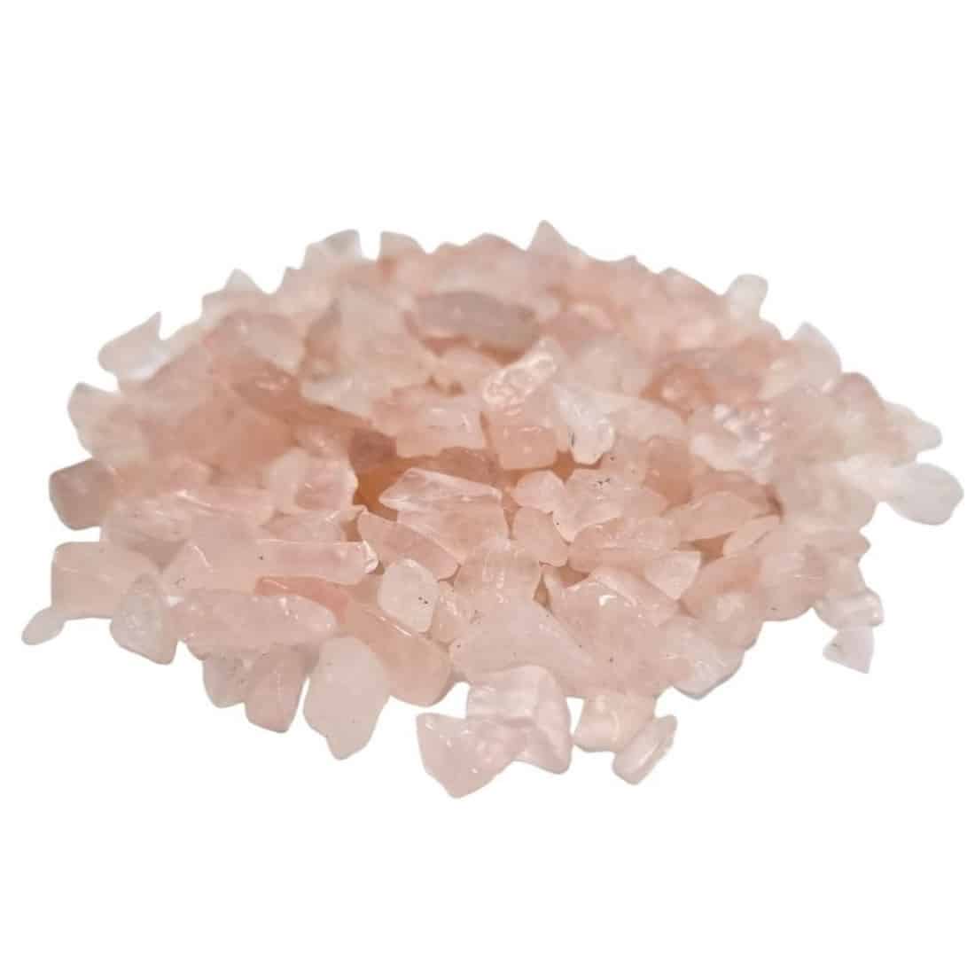 Rosenkvarts chips præsenterer en lyserød farvetone med varierende nuancer fra sart pastelmørk til dybere rosa. De små, ujævne sten har en glat overflade og et let transparent udseende. Nogle chips har naturlige sprækker og uregelmæssigheder, hvilket giver et organisk præg. Stenene ligger spredt, hvilket fremhæver deres forskellige former og størrelser.