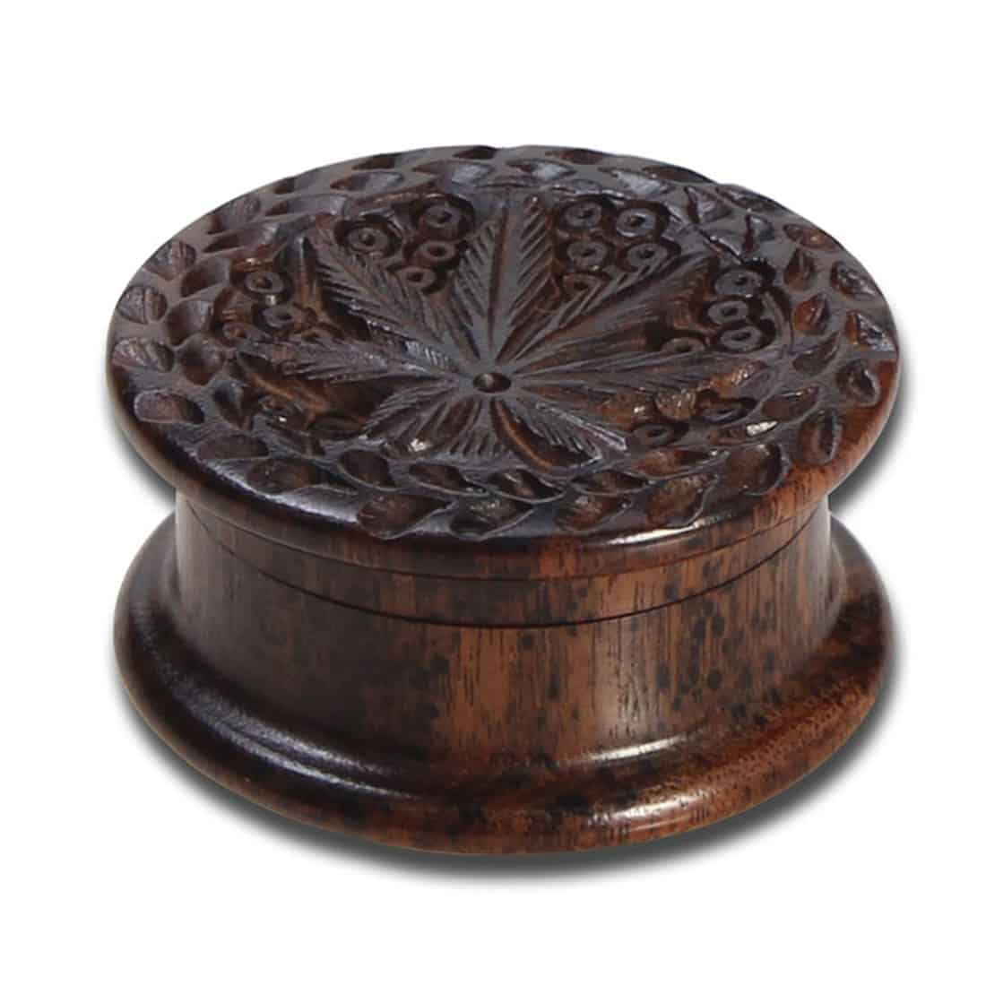 En trægrinder i palisandertræ præsenteres med en glat, dybbrun overflade, der fremhæver de naturlige åre og teksturer. Den har en rund form med en diameter på 40 mm og er udsmykket med detaljeret udskæring, der tilføjer en dekorativ dimension. Kanten er let buet, hvilket giver et elegant og organisk udtryk.