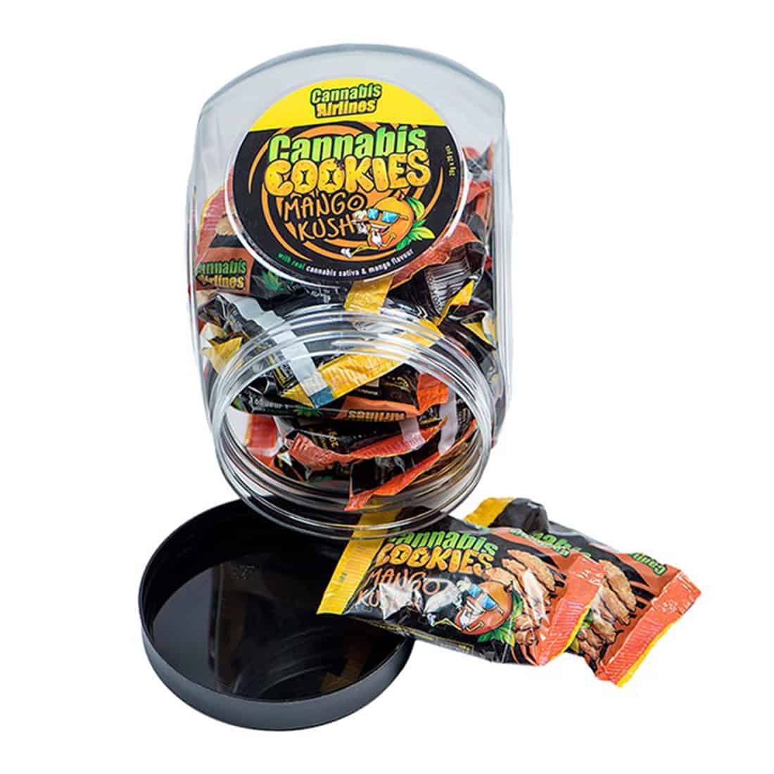 En pakke med cannabis-infuserede hamp småkager præsenteres med et farverigt design. Forsiden har en grøn baggrund med grafiske elementer i orange og gule nuancer, der fremhæver mango-kush temaet. Småkagerne er indpakket i en gennemsigtig sektion, der afslører den brune, sprøde tekstur. Øverste del indeholder tydelig tekst og symboler, der angiver indholdets art.