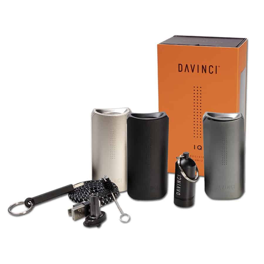 Da Vinci IQ vaporizer præsenterer et kompakt, firkantet design med bløde kanter. Overfladen er dækket af en mat, sort finish med en let tekstur. På forsiden ses en digital skærm og en knap, mens siden har ventilationsåbninger. Toppen er udstyret med en skruelåg, der afslører en keramisk urtkammer. Enheden har tydelige linjer og en minimalistisk æstetik.