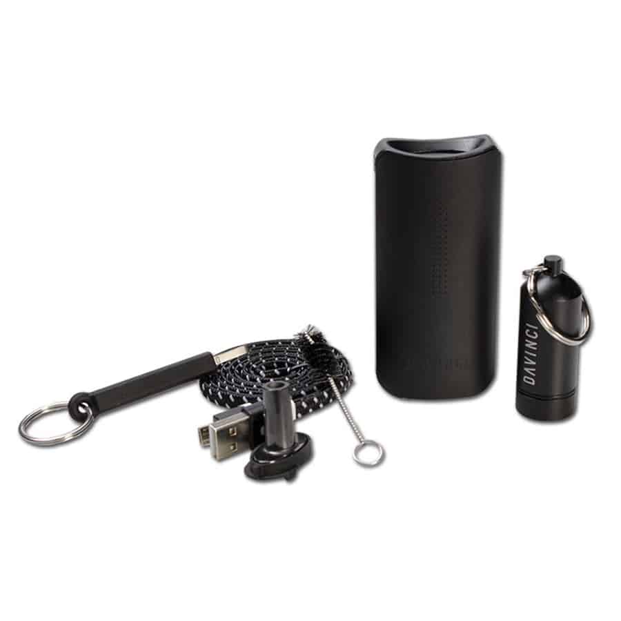 En kompakt vaporizer præsenteres i en mat, sort overflade med bløde kurver. Den har en digital skærm, der viser temperatur og tidsindstillinger, omgivet af en metalramme. To knapper er placeret på fronten til justering. En glat, ergonomisk form gør det let at holde, mens en lysere, grå bund fremhæver designet.