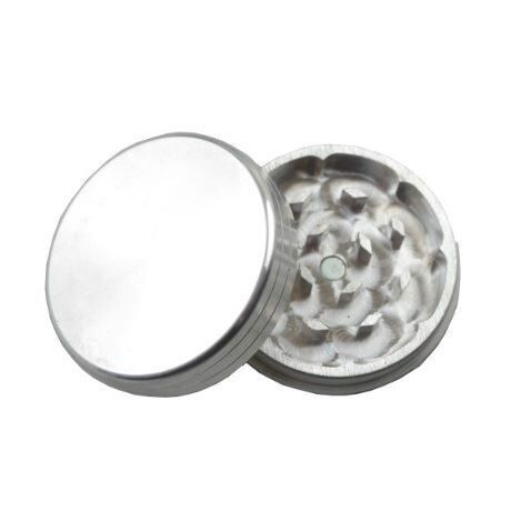 En sølvfarvet kværn med to dele præsenterer sig med en glat, metallisk overflade. Den øverste del har en skruefunktion til at holde de to sektioner sammen. Indvendigt er der skarpe tænder, der er designet til at male materialer. Kværnen har en kompakt, cylindrisk form med en rund base og en let buet top.