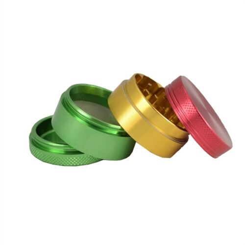 En metal grinder præsenterer sig med en farverig Rasta-inspireret design, domineret af rød, gul og grøn. Den har en cirkulær form med en glat overflade og en skinnende metalfinish. Øverste del er udstyret med en skarp tandstruktur, mens siderne har små, indgraverede detaljer. Grinderens knap til åbning er placeret centralt, hvilket muliggør nem adgang.