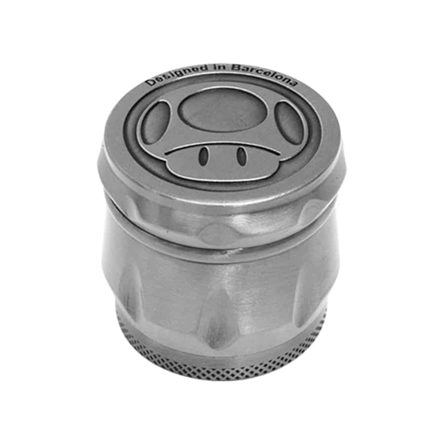 En sølvfarvet kværn i en kompakt, rund form præsenterer sig med en præget svampeformet tekstur på overfladen. Kværnen har en glat, skinnende finish, der reflekterer lys. Den er udstyret med en skrueknap i midten og en lavere del med små perforeringer, der muliggør en jævn kværning af indholdet. Kværnen har en elegant og moderne fremtoning.