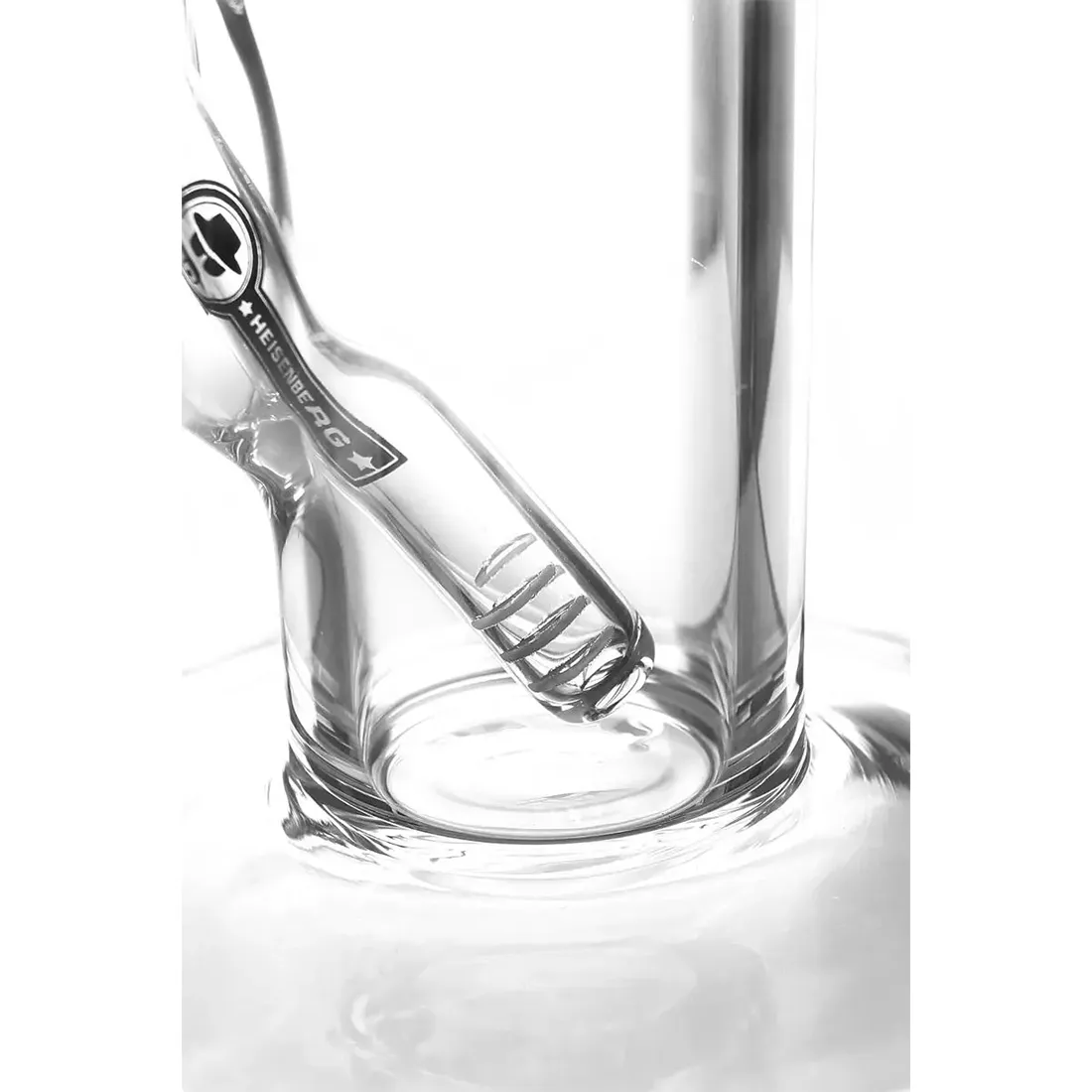 En gennemsigtig bong i klart glas med en slank, cylindrisk form. Den har en buet hals og en bred base, der sikrer stabilitet. Indvendigt ses et vandkammer, der skaber bobler. Bongen har en metallisk skål med perforeringer og en silikoneledning i mørkeblå. Overfladen er glat med lette refleksioner, og der er ingen synlige dekorative elementer.