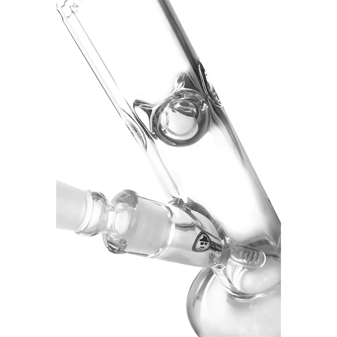 En bongs struktur fremstår i klart glas med en cylindrisk form og en bred bund. Den har en nedadgående rørføring, der ender i en skål til tobaksprodukter. Overfladen er glat med en let buet hals, og der er indsat farverige mønstre i blåt og hvidt. En lille, aftagelig perkolator er synlig, og der er en tæt pasform mellem dele.