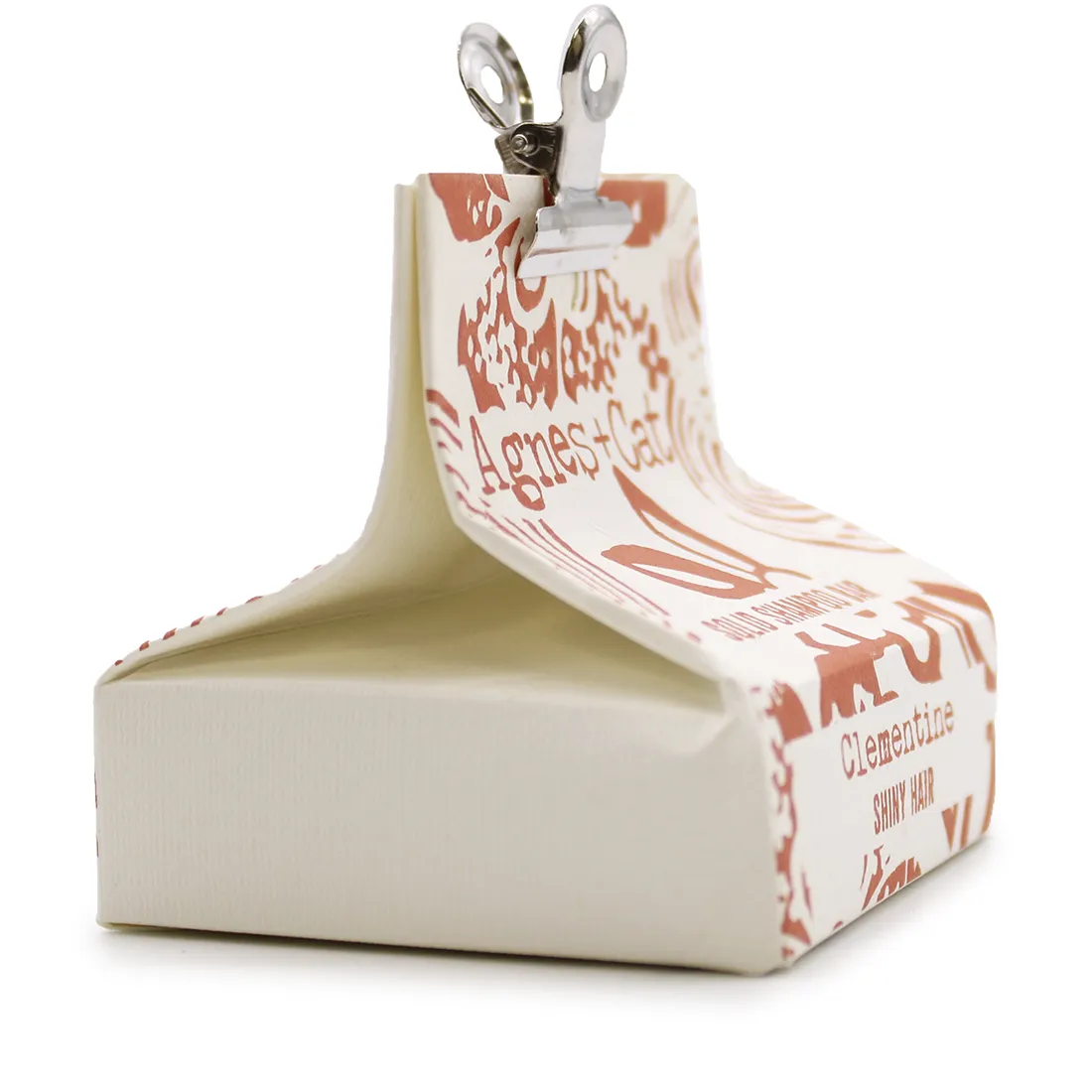 En solid shampoo-bar præsenteres med en rund form og en glat, ensartet overflade. Farven er en varm, gylden orange nuance. Teksturen er fast og kompakt, uden synlige luftbobler. Ingen synlige ingredienser eller skrifttyper er til stede. Shampoo-baren hviler på en lys, neutral overflade, hvilket fremhæver dens farve og form.