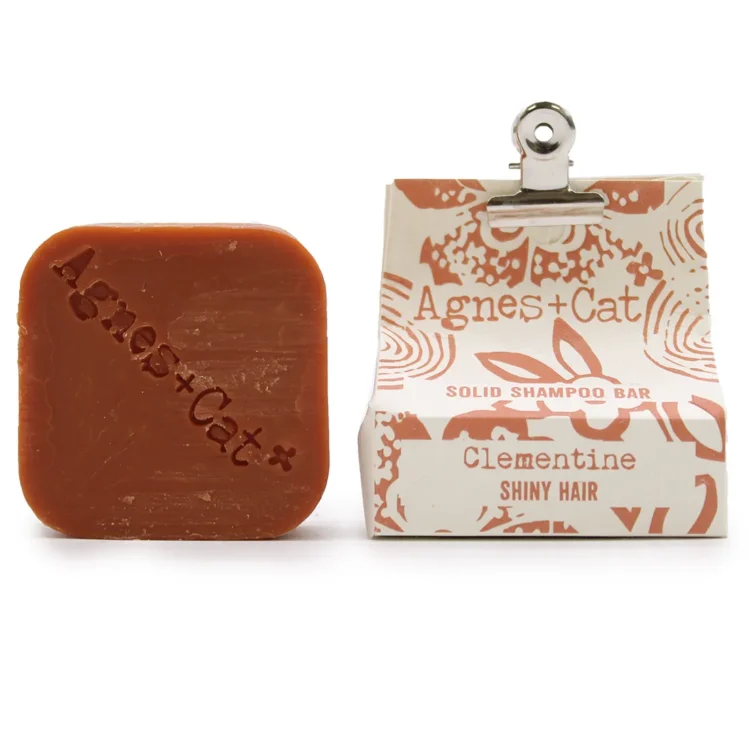 En solid shampoo bar med en rund form, prydet med en lys orange farve. Overfladen er glat og ensartet, uden synlige urenheder. En delikat struktur kan anes, som tilføjer en let mat finish. Ingen synlige emballager eller etiketter er til stede, hvilket giver et minimalistisk udtryk. Størrelsen er håndholdt og kompakt.