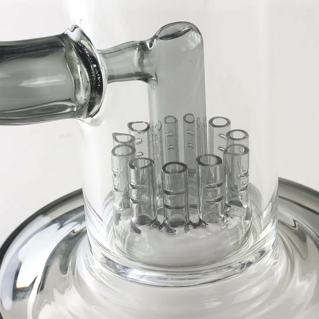 En høj, gennemsigtig bong fremstillet af klart glas med en glat overflade. Den har en cylindrisk form med en krum hals og en bred bund for stabilitet. Indvendigt er der en perkolator med flere små huller, der skaber bobler. Bongen prydes af en farverig, uregelmæssig mønstring langs kroppen, og der er en afrundet skål til tobak.