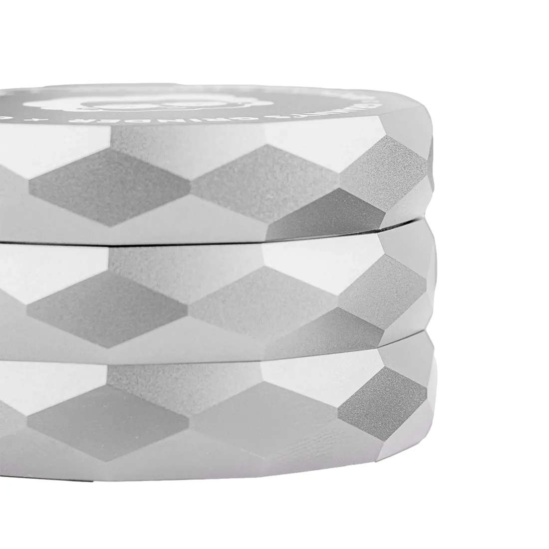 Grinderen er lavet af metal med en blank sølvfinish, der reflekterer lys. Den har en hexagonal form med skarpe kanter og er 55 mm i diameter. Overfladen viser fine ridser og et let struktureret mønster. Øverst er der et skruelåg med en præcis pasform. Indvendigt ses skarpe tænder til formaling, der er jævnt fordelt.