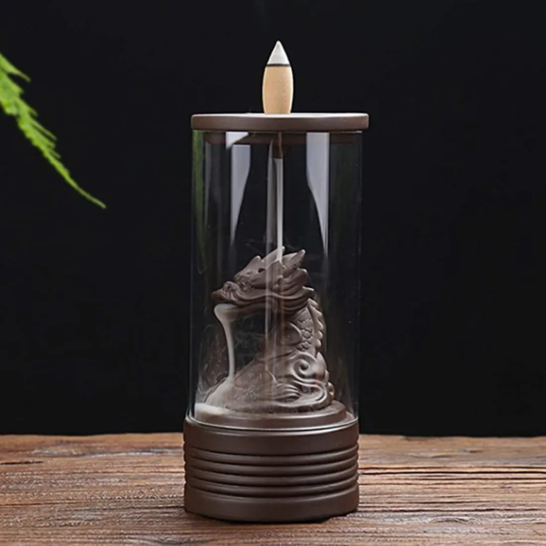 En brænder i form af en drage, fremstillet af keramik med en glat, glinsende overflade. Dragen har detaljerede skalaer og en elegant krop, der slynger sig nedad. Vandfaldene, der strømmer fra dragens mund, har en gennemsigtig og let blåtone, mens den nederste del er dekoreret med små, naturlige klippeformationer. En kombination af farver fra dyb grøn til brun pryder basen.