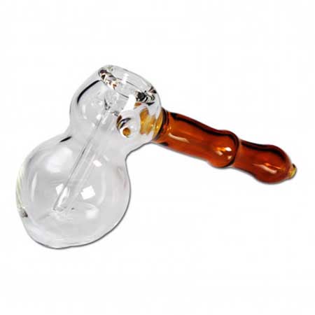 En rund, gennemsigtig glasflaske med en dyb amberfarve dominerer. Flasken har en elegant form med en bred bund, der smalner ind mod en slank hals. På toppen sidder en nærmest kugleformet prop, der har en let struktur. Overfladen er glat, og reflekterer lyset i varme nuancer, hvilket giver et indtryk af dybde og glans.