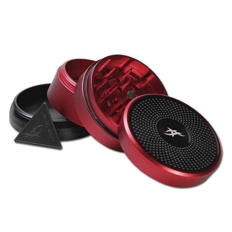 En rød kvadratisk kaffekværn med en mat overflade præsenterer sig med en sort drejeknap øverst. Kværnens front har en gennemsigtig plastlåge, der giver indsigt til det indre kvarter med metalbladesynkronisering. Den firkantede base har afrundede hjørner, og der er små luftventiler på siderne, hvilket giver et strømlinet udtryk.