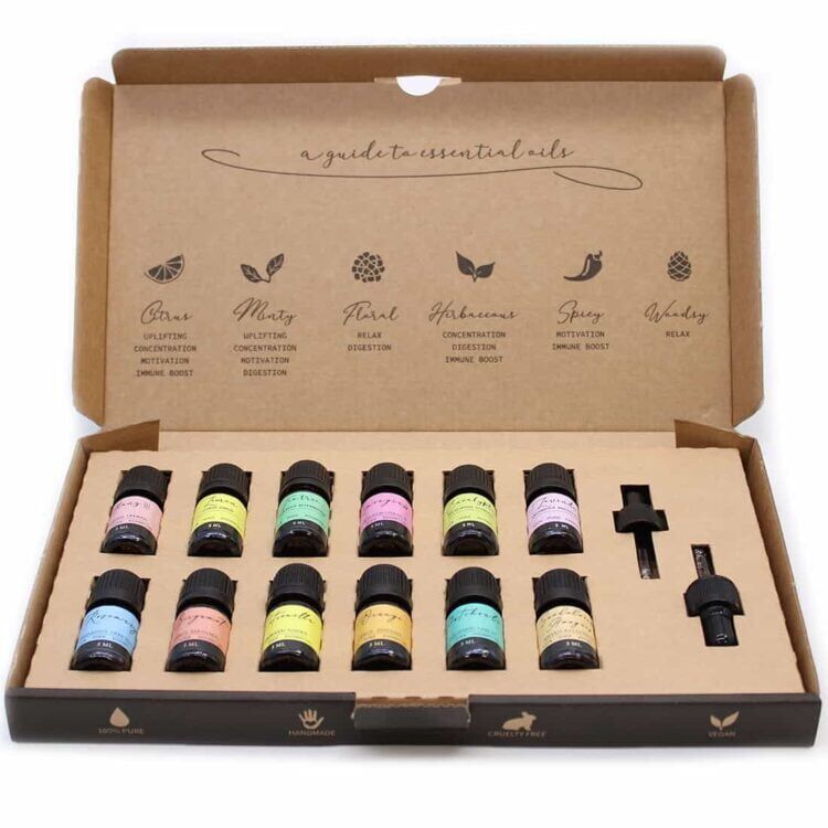 En transparent flaske med en mørkeblå væske indeholder en æterisk olie. Flasken har en rund, slank form og en gylden korkprop. Etiket i hvidt og grønt pryder flaskens front med tekst og detaljerede illustrationer. En guldkant omkranser etiketten, og flaskens bund er bredere end toppen, hvilket giver stabilitet. Refleksioner fra lyset fremhæver væskens glans.