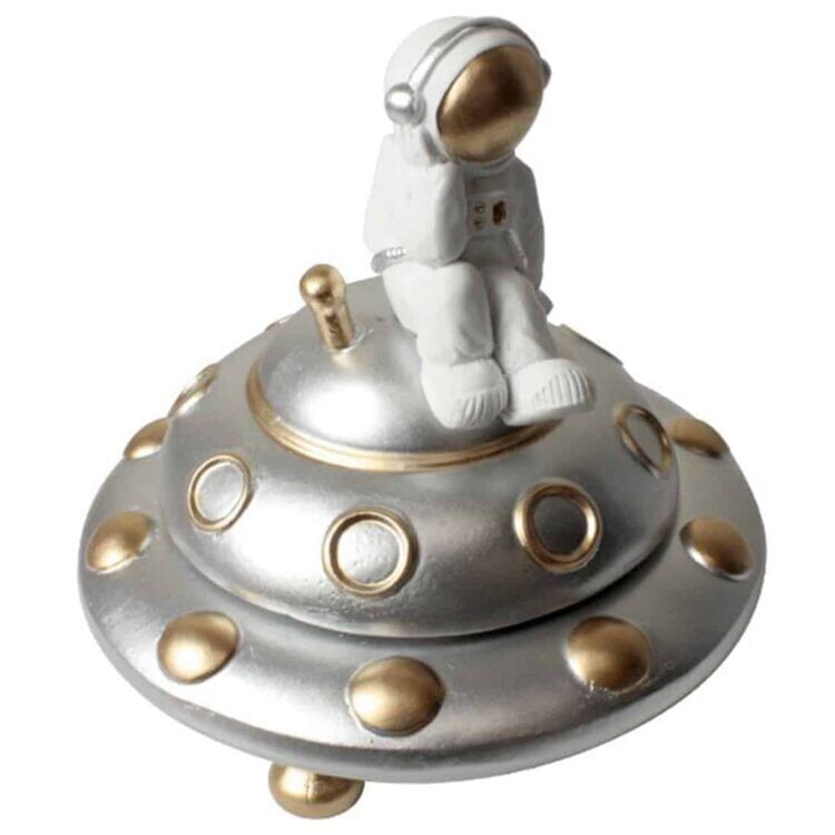 En skulpturel askebæger i form af et rumskib præsenterer sig med glatte, kurvede linjer og en metallic grå overflade. Det har en detaljeret cockpit sektion med en transparent kuppel, der giver indblik til det indre. Bunden er bred og stabil, mens der er små, fine detaljer som motorer og vinger, der tilføjer dybde og karakter.