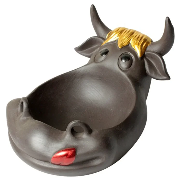 Et askebæger i klar glasform med en rund bund og let opadgående kant. Overfladen er glat med en let buet form, der giver en elegant silhuet. Indgraveringen af en glad ko dekorerer forsiden, mens et lille hul i kanten fungerer som en holder til cigaretter. Farven er gennemsigtig, hvilket fremhæver dets enkle design.