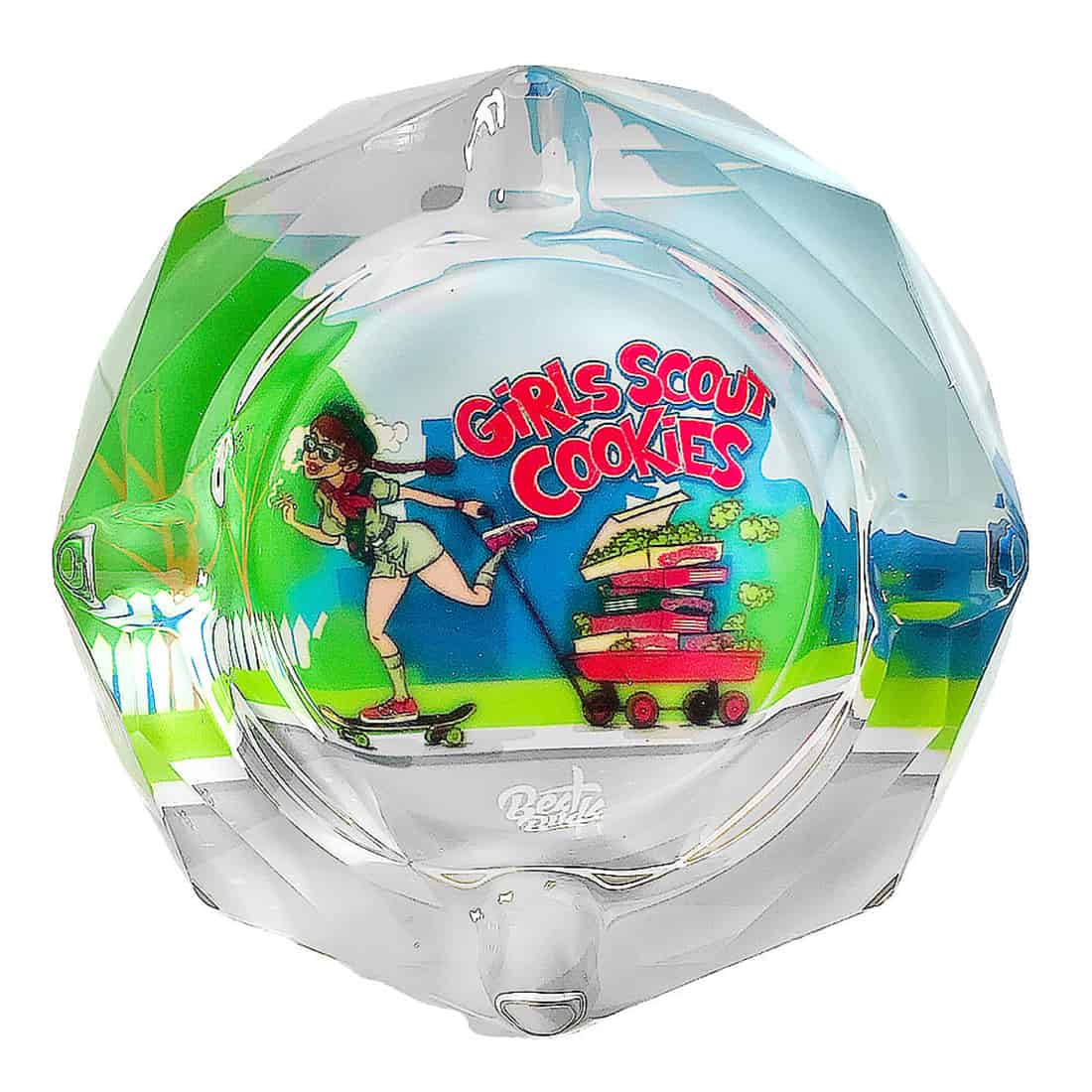 En klar, krystalagtig askebæger præsenterer sig med en geometrisk, facetteret overflade, der fanger lys og skaber glimt. Bunden er flad og stabil, mens siderne er let skrå og prydet med et indviklet mønster. Farven er gennemsigtig med en let blålig nuance, hvilket tilføjer dybde og elegance til designet.