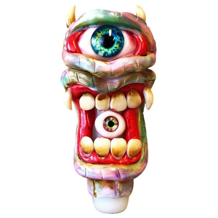 En sort glasrørformet genstand præsenterer sig med en glat, skinnende overflade. Den har en unik struktur med en grusom, monstruøs ansigtstræk, herunder store, skræmmende øjne og en åben mund. Detaljer som små knopper og ujævne kantlinjer tilføjer dybde. Røret måler 150 mm og har en buet form, der afsluttes med en bred åbning.