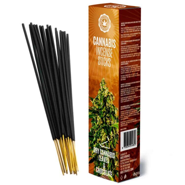 Cannabisrøgelsespinde ligger i en bunke, omgivet af tørrede cannabisblade, der har en dyb grøn farve med lette nuancer af brun. Ved siden af findes et stykke chokolade, der er mørkt og glinsende, med en glat overflade. Mønstret på chokoladebaren er opdelt i firkanter, hvilket skaber en strukturel kontrast til de bløde blade.