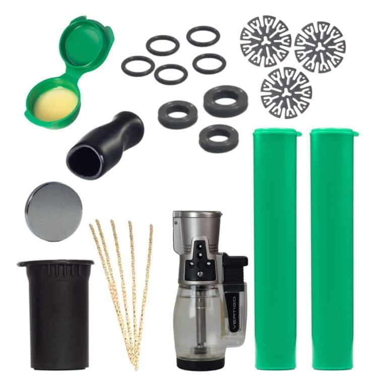 Dynavap Dynakit Deluxe præsenterer en kombination af metal og glas med en glat, sølvfarvet finish. Sættet omfatter en rørformet enhed med en indviklet mønsterstruktur og en krystalagtig glasbeholder. Flere komponenter er arrangeret i en sort, struktureret taske med lynlås, der indeholder plads til hver del, hvilket sikrer en kompakt opbevaring.