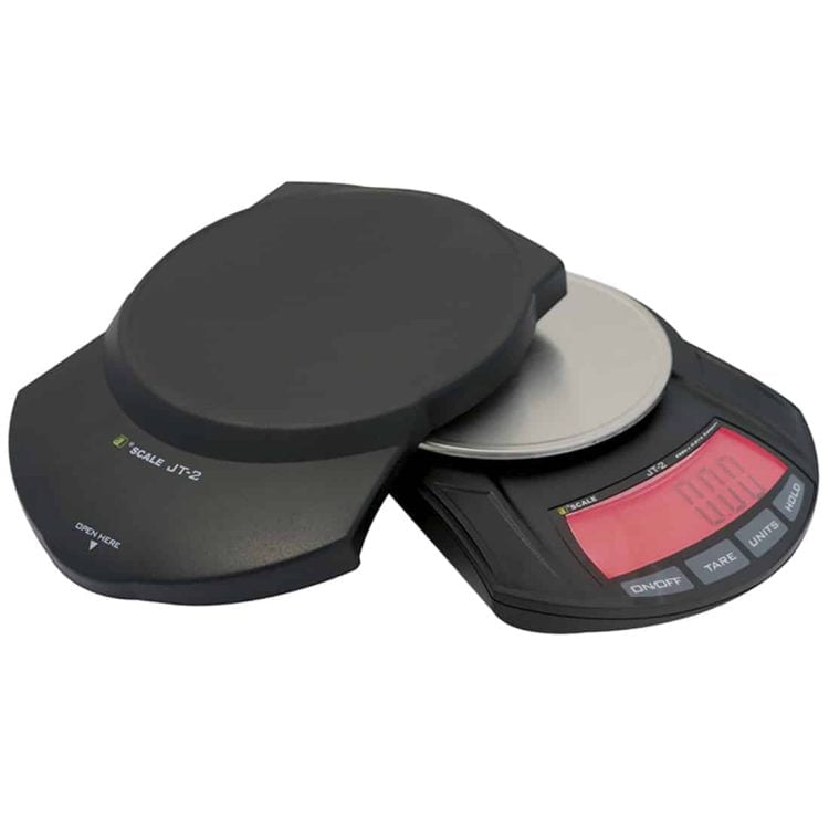 En rund, metalgrå kasse med en glat overflade og en diameter på cirka 35 cm. Kassen har en flad top og bunden er let hævet. På toppen er der en lille, sort plastknap, omgivet af en fin, sort gummitætning. Kassen er designet med en minimalistisk æstetik, der fremhæver dens funktionelle udtryk.