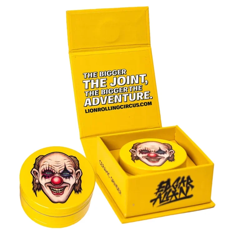 En keramisk kværn med en diameter på 50 mm præsenterer sig med en glat, glansfuld overflade i nuancer af brun og beige. Mønstret er inspireret af en cirkuslignende æstetik, hvor detaljerede lion-illustrationer og forskellige geometriske figurer skaber visuel interesse. Kværnen har en metalknap til åbning og lukning samt små udskæringer for nem greb.