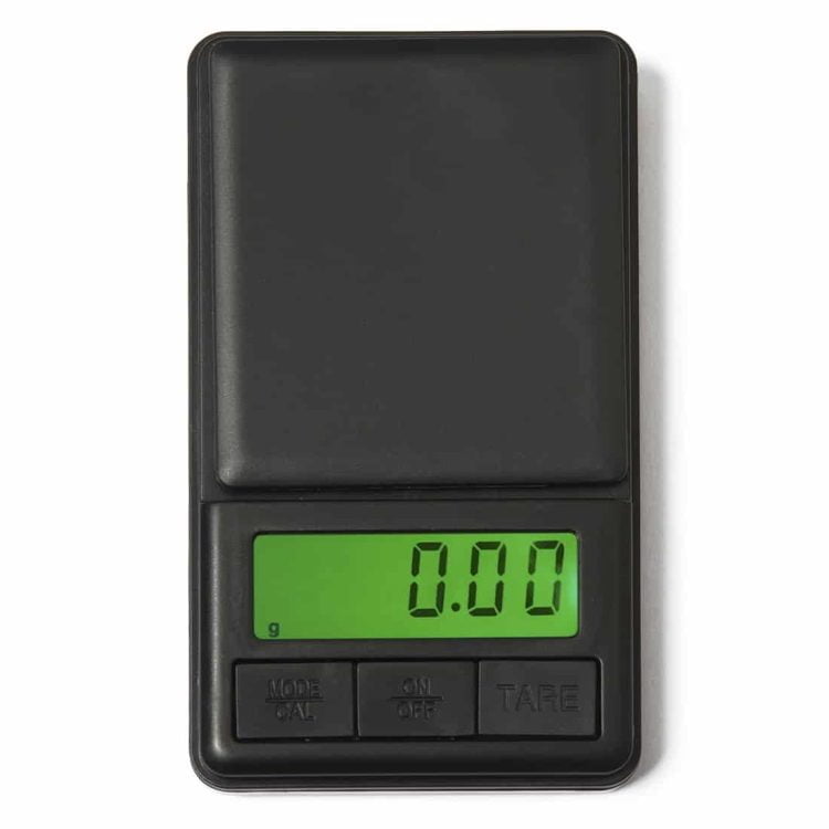 Et rektangulært metalvægt med en blank overflade pryder midten af en hvid baggrund. Vægten har tydelige tal i en sort skrifttype, som angiver vægtmålinger. Den har en rund, sort drejeknap øverst, omkranset af en sølvfarvet ring. Under vægten er der en sort gummibase, der sikrer stabilitet.