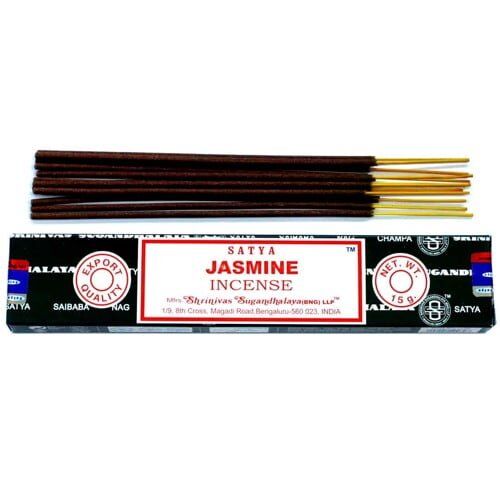 En pakke med røgelse i papir med et blomstermotiv pryder forsiden. Farverne spænder fra lysegrønne nuancer til dybe lilla og hvide blomster. Teksten er trykt i en elegant skrifttype, og der er et symbol, der angiver indholdet. Pakken er rektangulær og har en perforeret åbning øverst, der giver adgang til røgelsen.