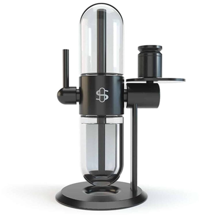 En klar, cylindrisk bong lavet af glas pryder midten, med en glat overflade og let buede former. Den har en bred bund, der giver stabilitet, og en smal hals, der strækker sig opad. En skål til tobaksprodukter er placeret på siden, og en slange forbindes til bunden. Glasets gennemsigtighed fremhæver den indvendige struktur.