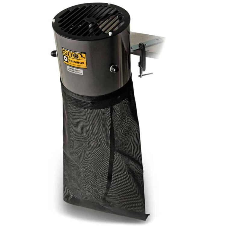 Trimbox er en rektangulær enhed med en mat, sort overflade og afrundede kanter. Den har en central åbning med en grå kant og små ventilationshuller. På forsiden findes en række knapper med forskellige symboler, der indikerer funktioner. Enheden står på fire små gummifødder, der sikrer stabilitet og beskytter underlaget mod ridser.