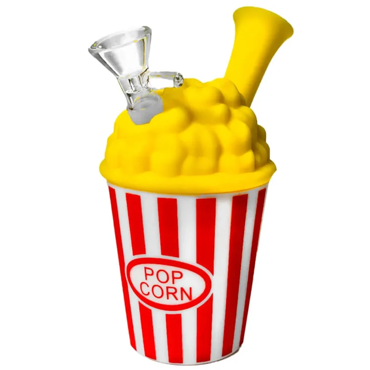 En silikonebong i en popcornbøtte-lignende form, måler 15 cm i højden. Den har en lys gul farve med en glat, blød tekstur. Bøttens overflade prydes af små, runde buler, der minder om popcorn. Der er en rund åbning øverst og en aftrækningsdyse i bunden, hvilket skaber en funktionel struktur.