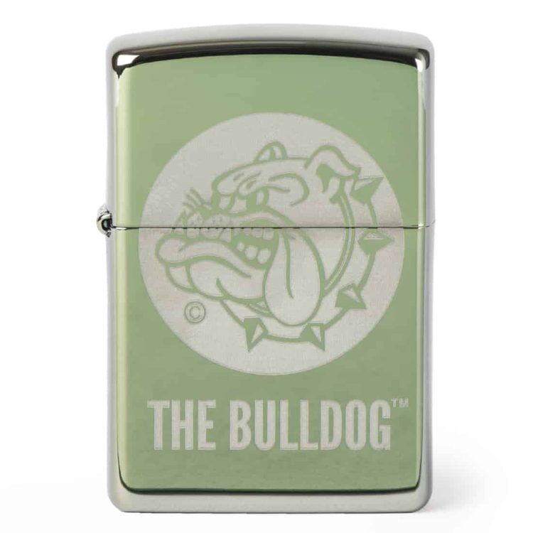 En højglans teal lighter er præsenteret med en detaljeret gravering af en bulldog på fronten. Lighterens overflade glitrer i lyset og fremhæver de glatte kurver og skarpe kanter. Baggrunden er neutral, hvilket får lighteren til at fremstå mere fremtrædende. Den har en klassisk form og en robust konstruktion, der indikerer holdbarhed.